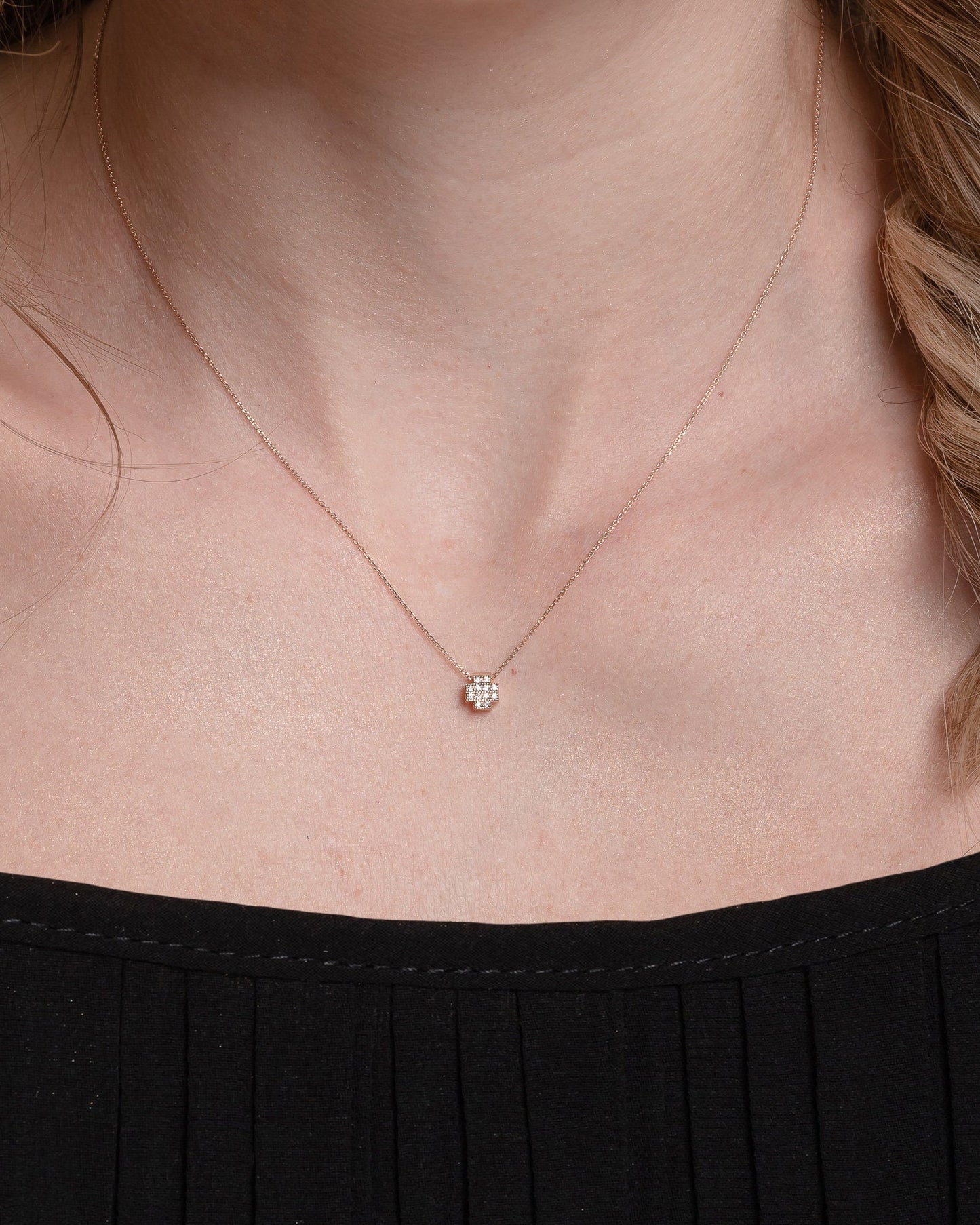 square cross necklace in 14k gold paved with white cubic zirconia stones for women worn by  a model 