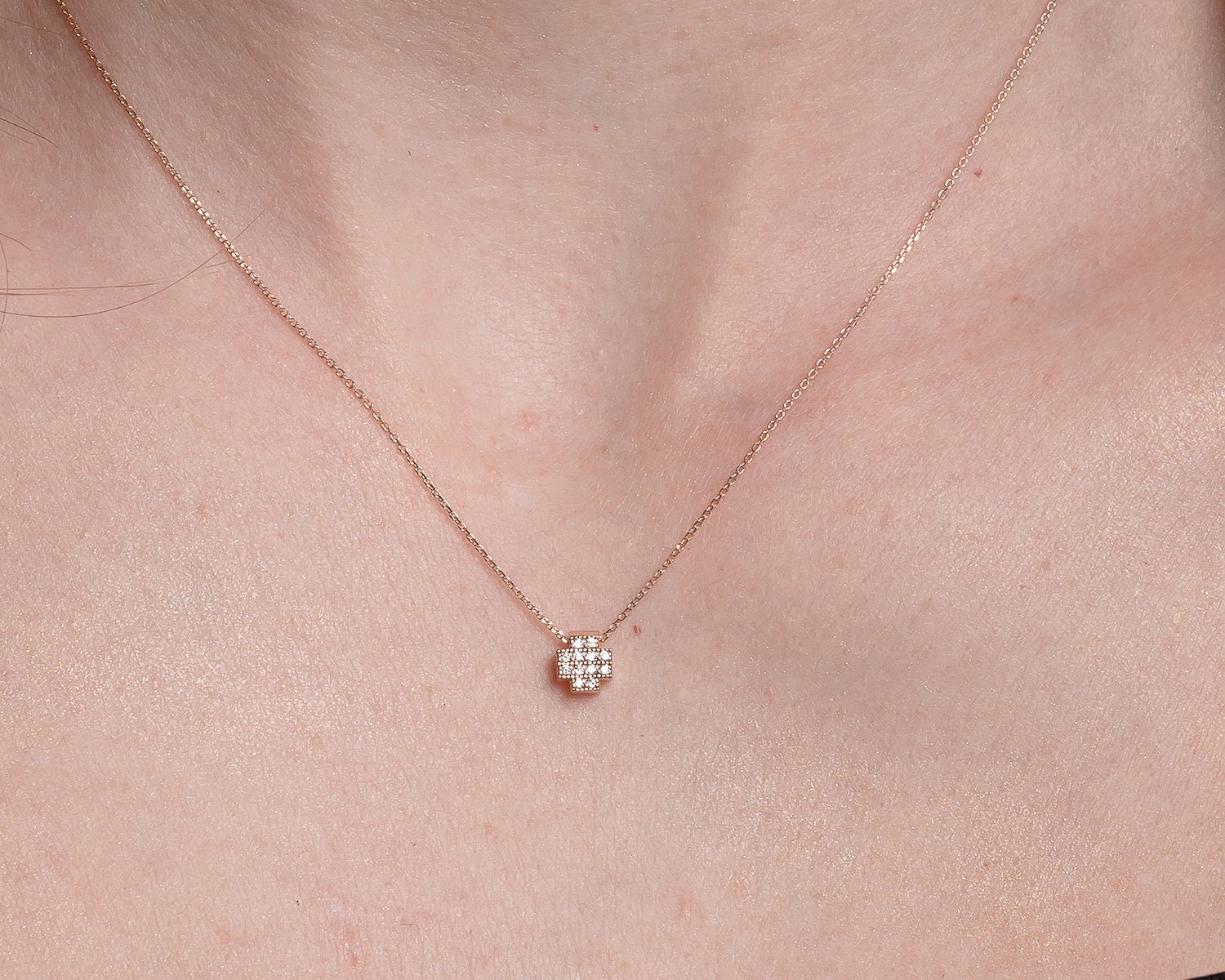 square cross necklace in 14k gold paved with white cubic zirconia stones for women worn by a model 