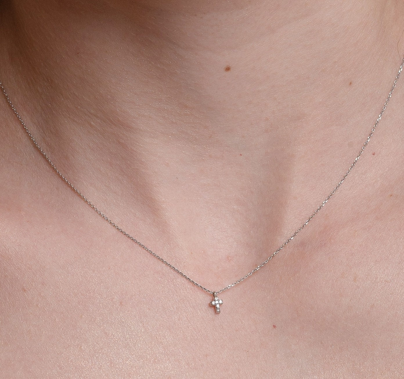 tiny diamond cross necklace in 14k white gold for women worn by a model 