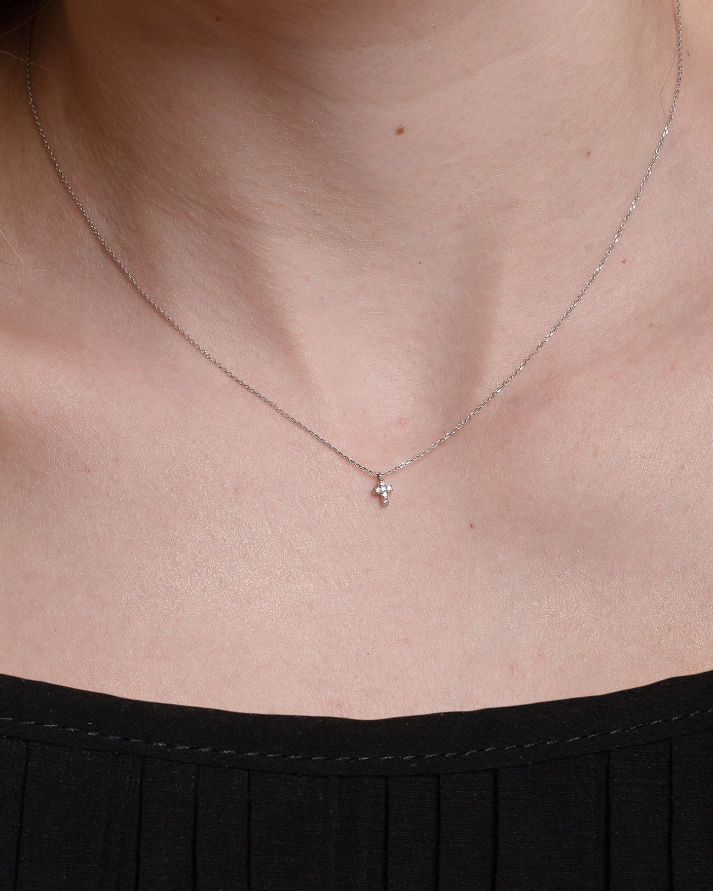 tiny diamond cross necklace in 14k white gold for women worn by a model 