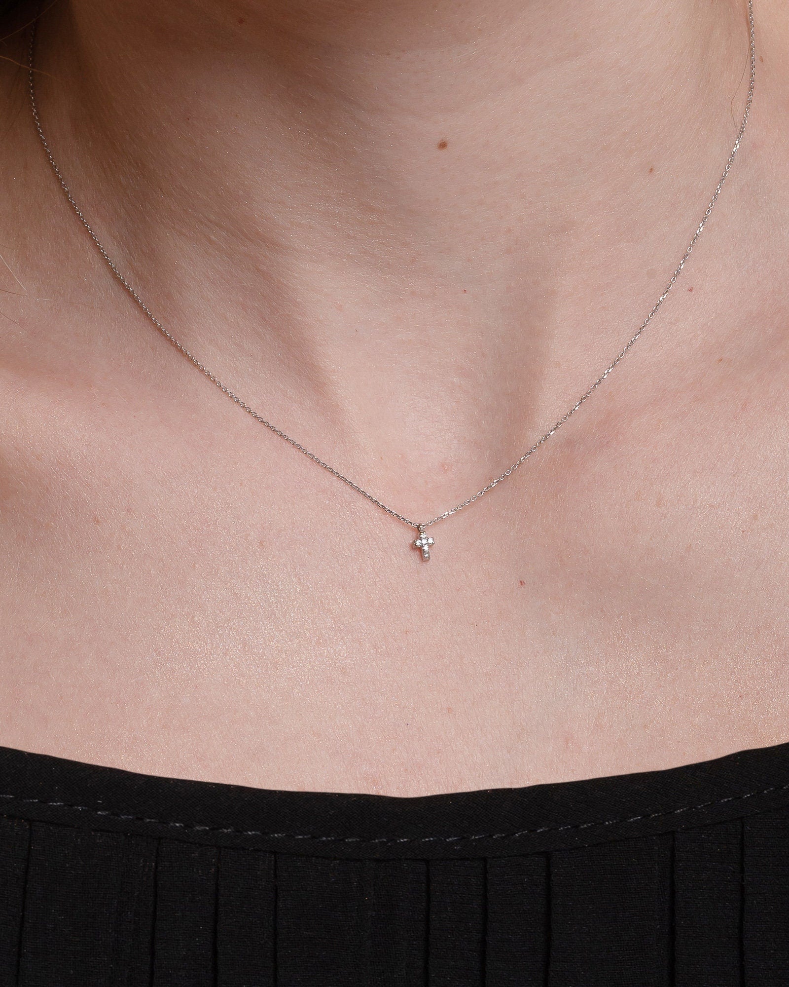 tiny diamond cross necklace in 14k white gold for women worn by a model 