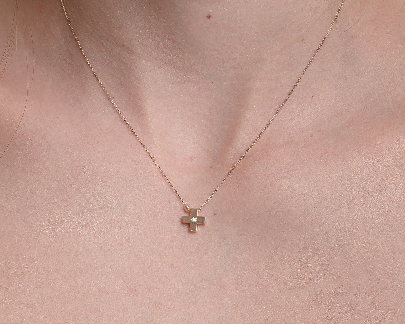 small diamond cross necklace with a small pearl in 14k yellow gold for women worn by a model 