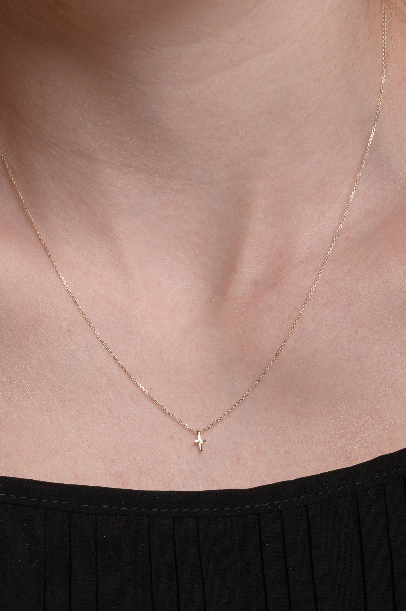 tiny diamond cross necklace in 14k yellow gold worn by a model 