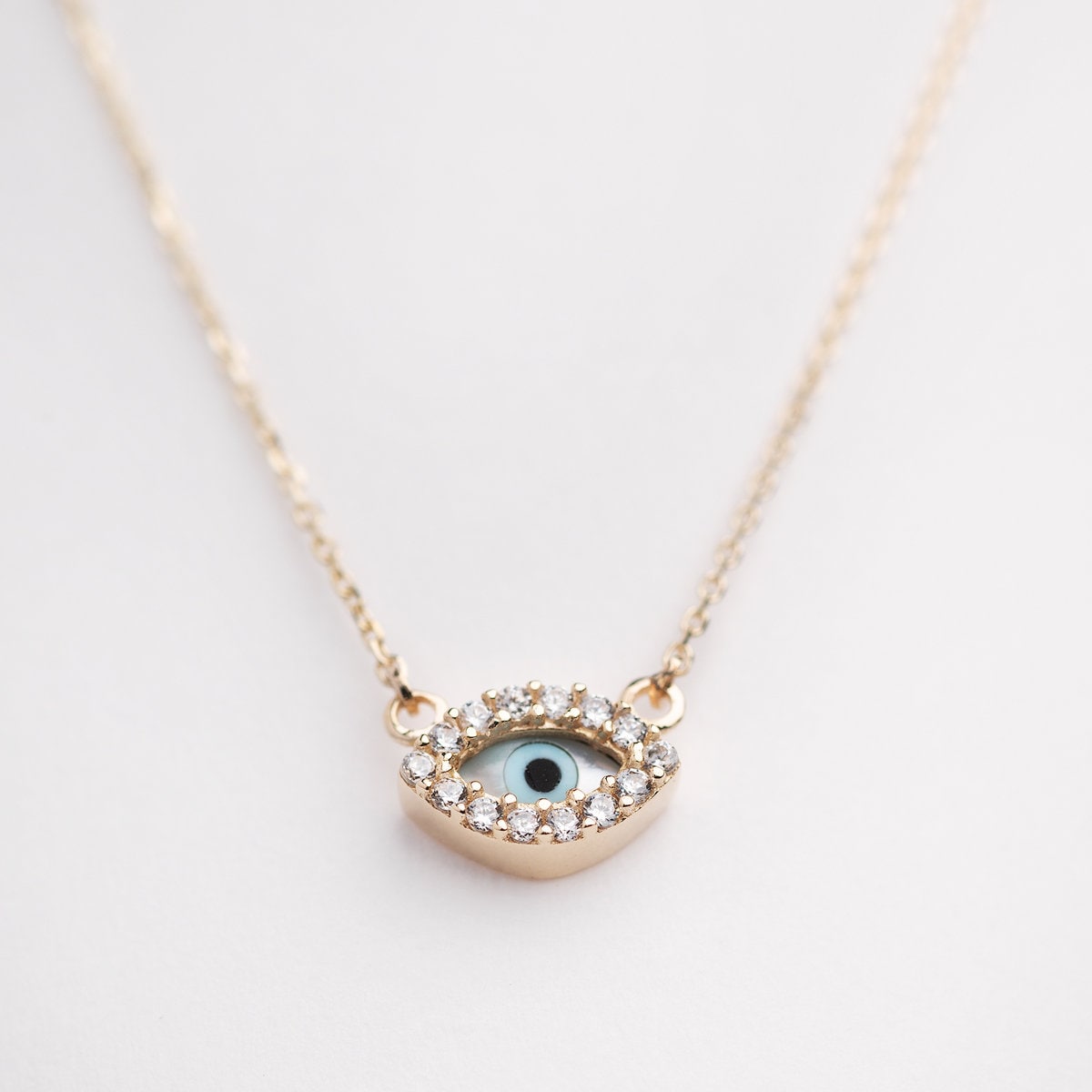 An oval-shaped evil eye necklace featuring mother of pearl and cubic zirconia stones, set in 14k gold for women.