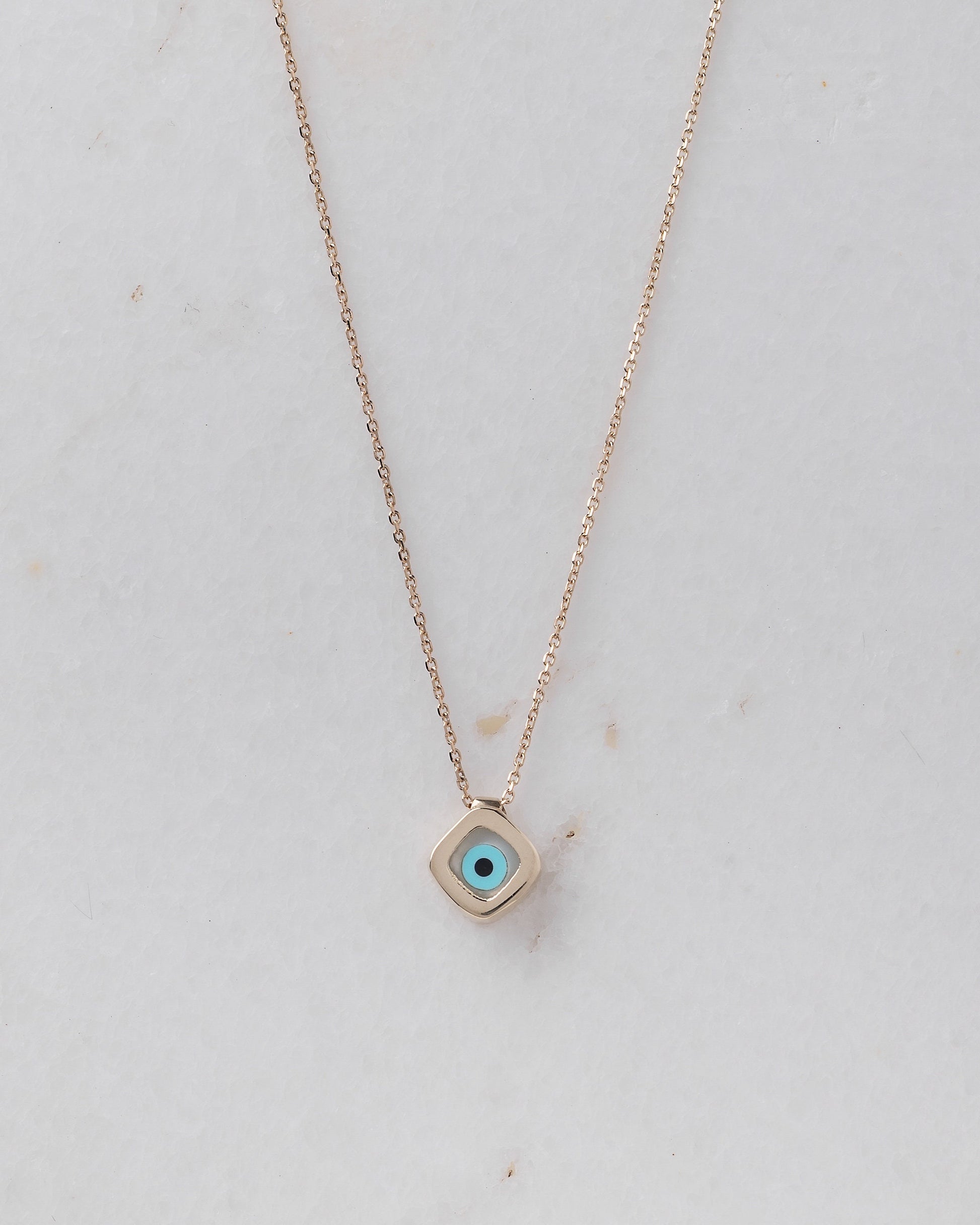 A mother-of-pearl evil eye necklace in 14k gold, fashioned in a rhombus shape.