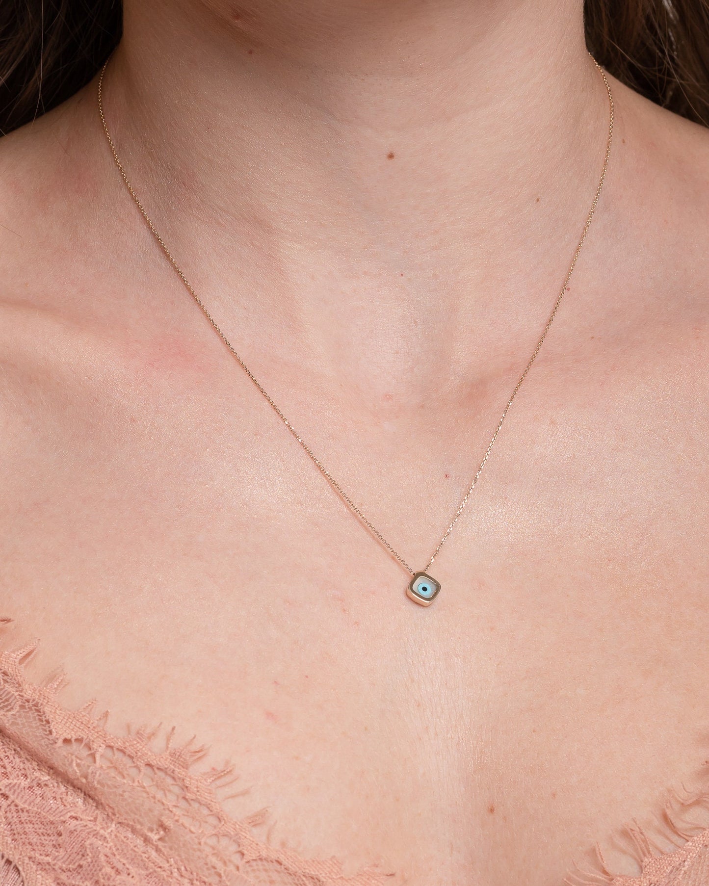 A mother-of-pearl evil eye necklace in 14k gold, fashioned in a rhombus shape worn by a model 