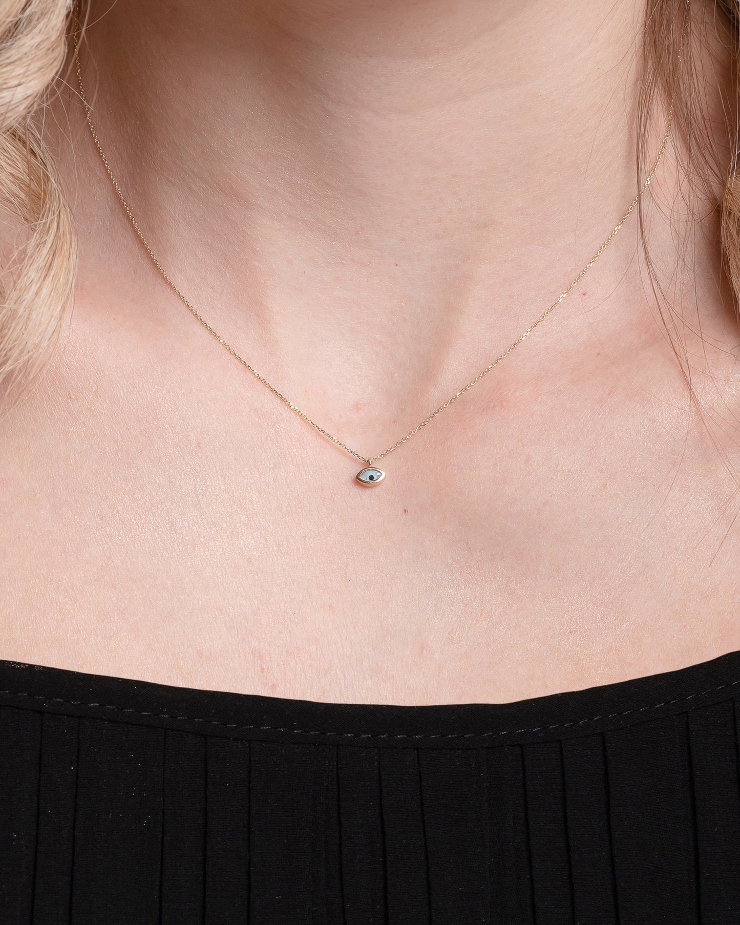 Tiny mother-of-pearl evil eye necklace in 14k gold for women worn by a model 