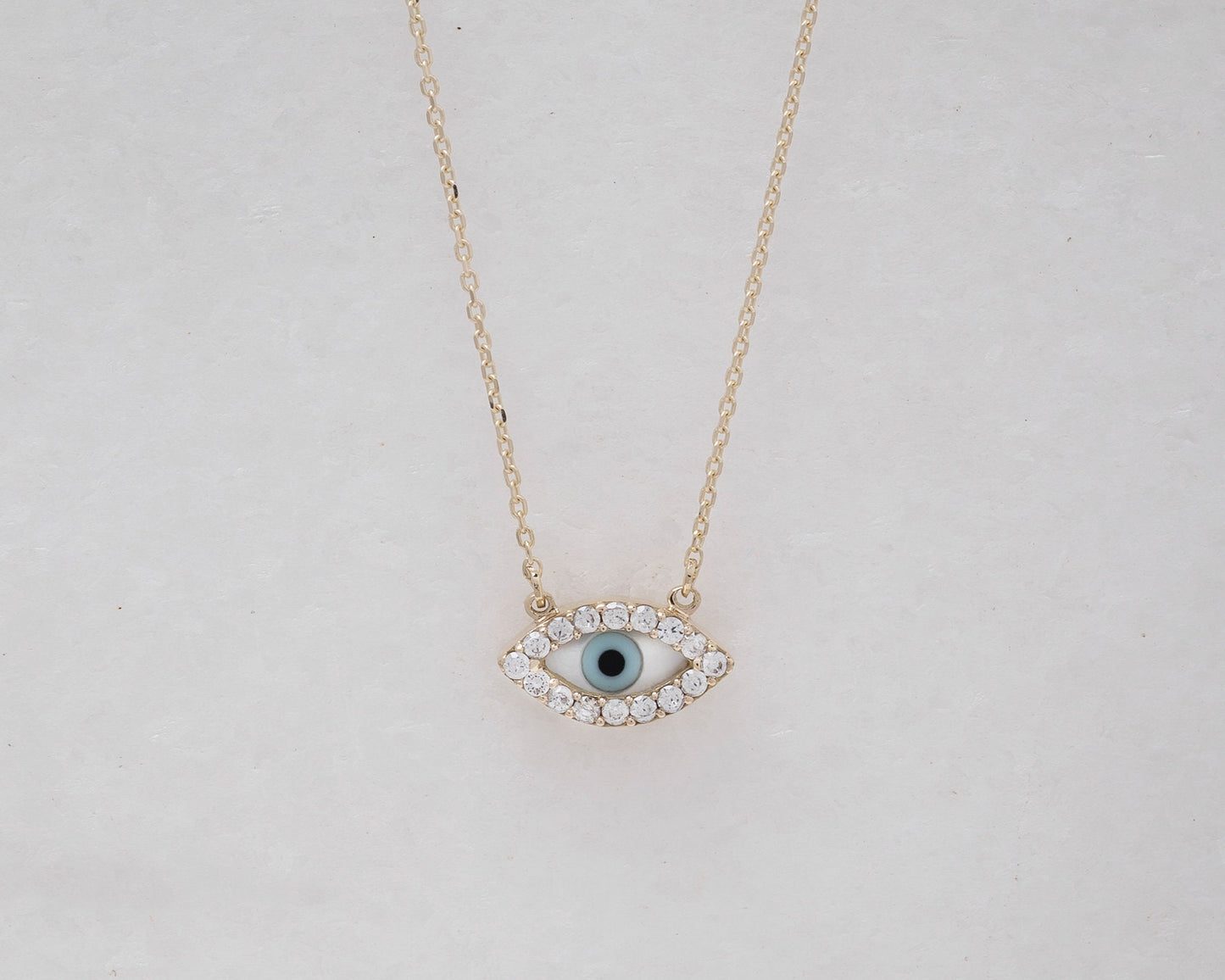 An oval-shaped mother of pearl evil eye necklace for women, crafted in 14k gold and adorned with cubic zirconia stones 