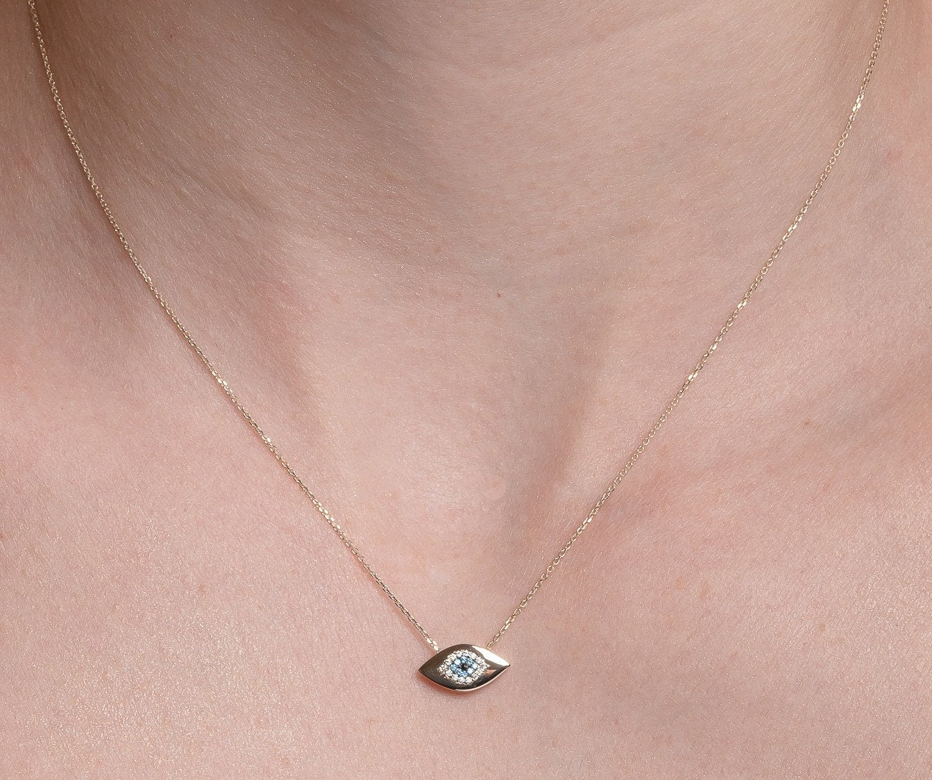 An oval-shaped evil eye necklace crafted in 14k gold and encrusted with cubic zirconia stones worn by a model 