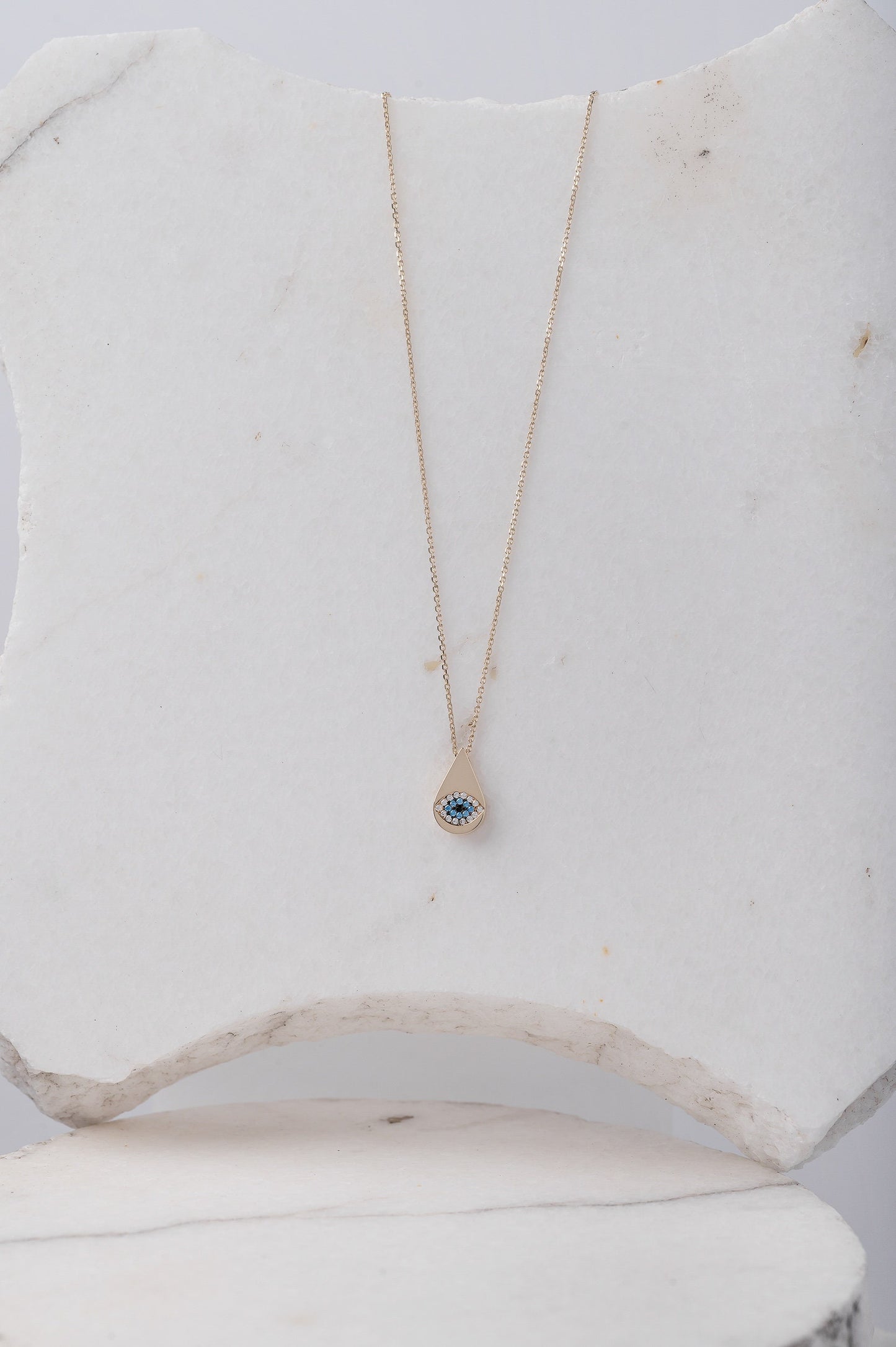 A drop-shaped evil eye necklace, encrusted with cubic zirconia stones and set in 14k gold.