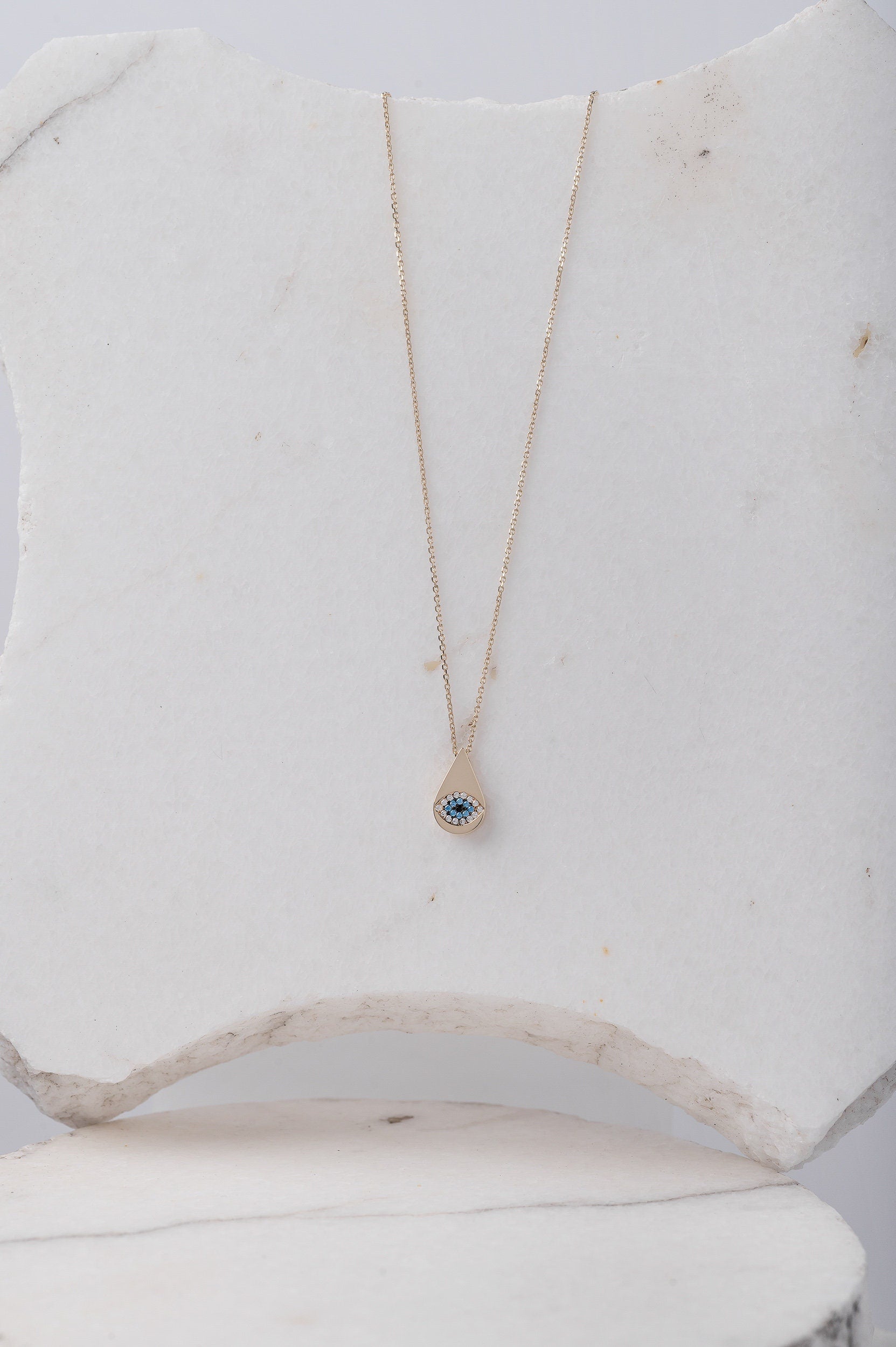 A drop-shaped evil eye necklace, encrusted with cubic zirconia stones and set in 14k gold.