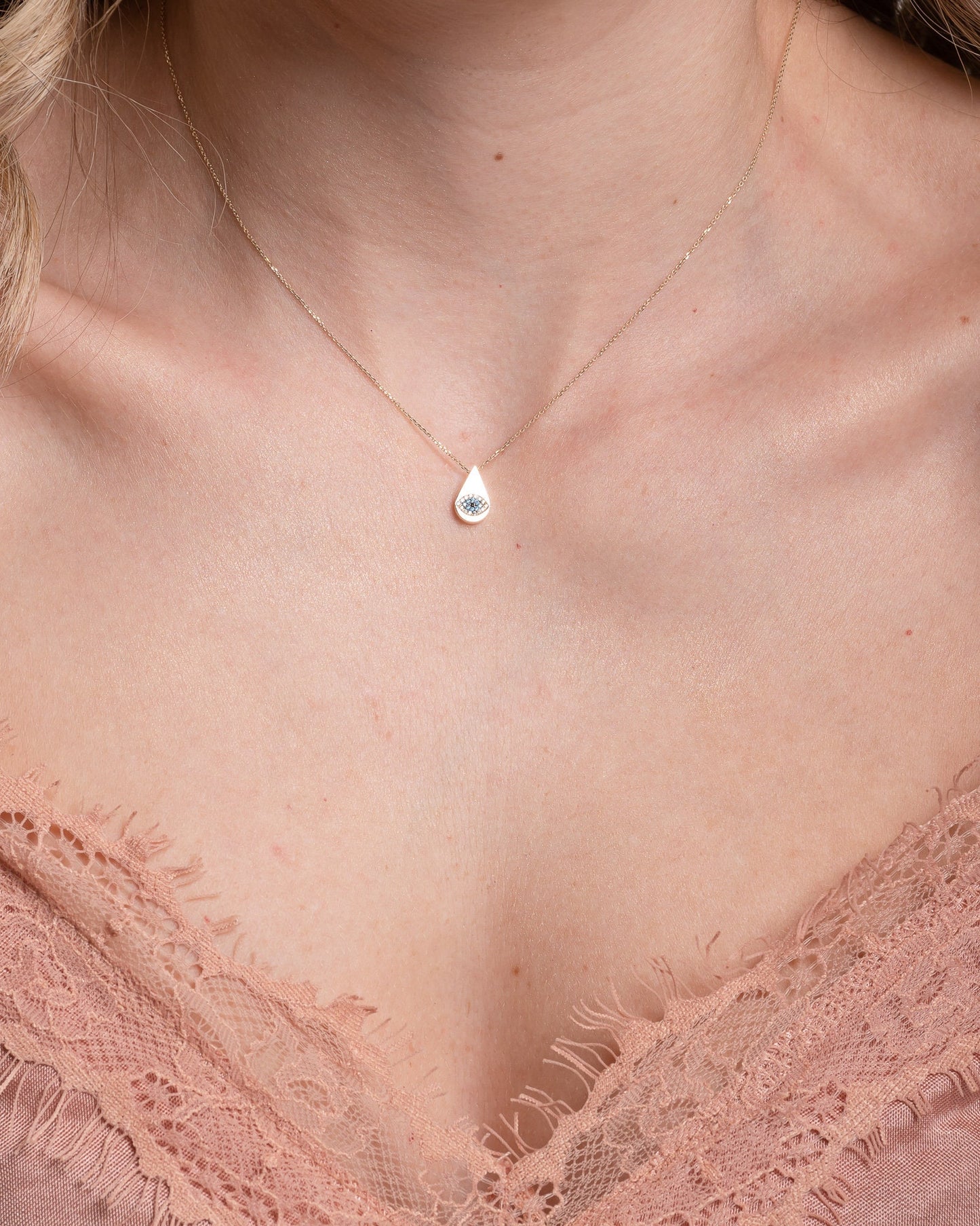 A drop-shaped evil eye necklace, encrusted with cubic zirconia stones and set in 14k gold worn by a model 
