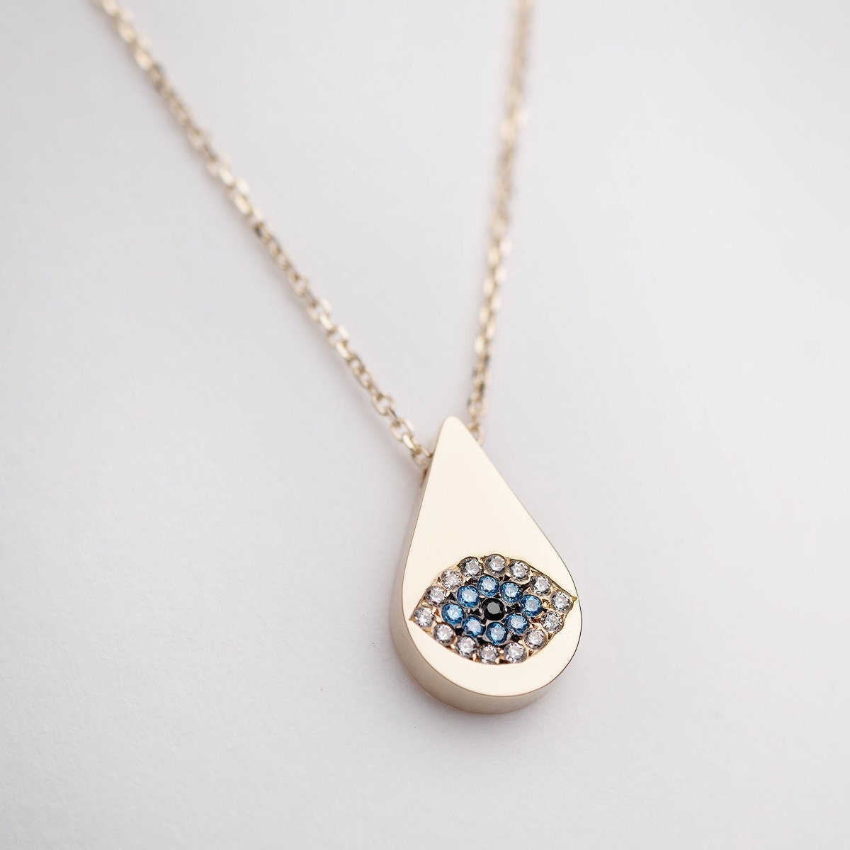 A drop-shaped evil eye necklace, encrusted with cubic zirconia stones and set in 14k gold.