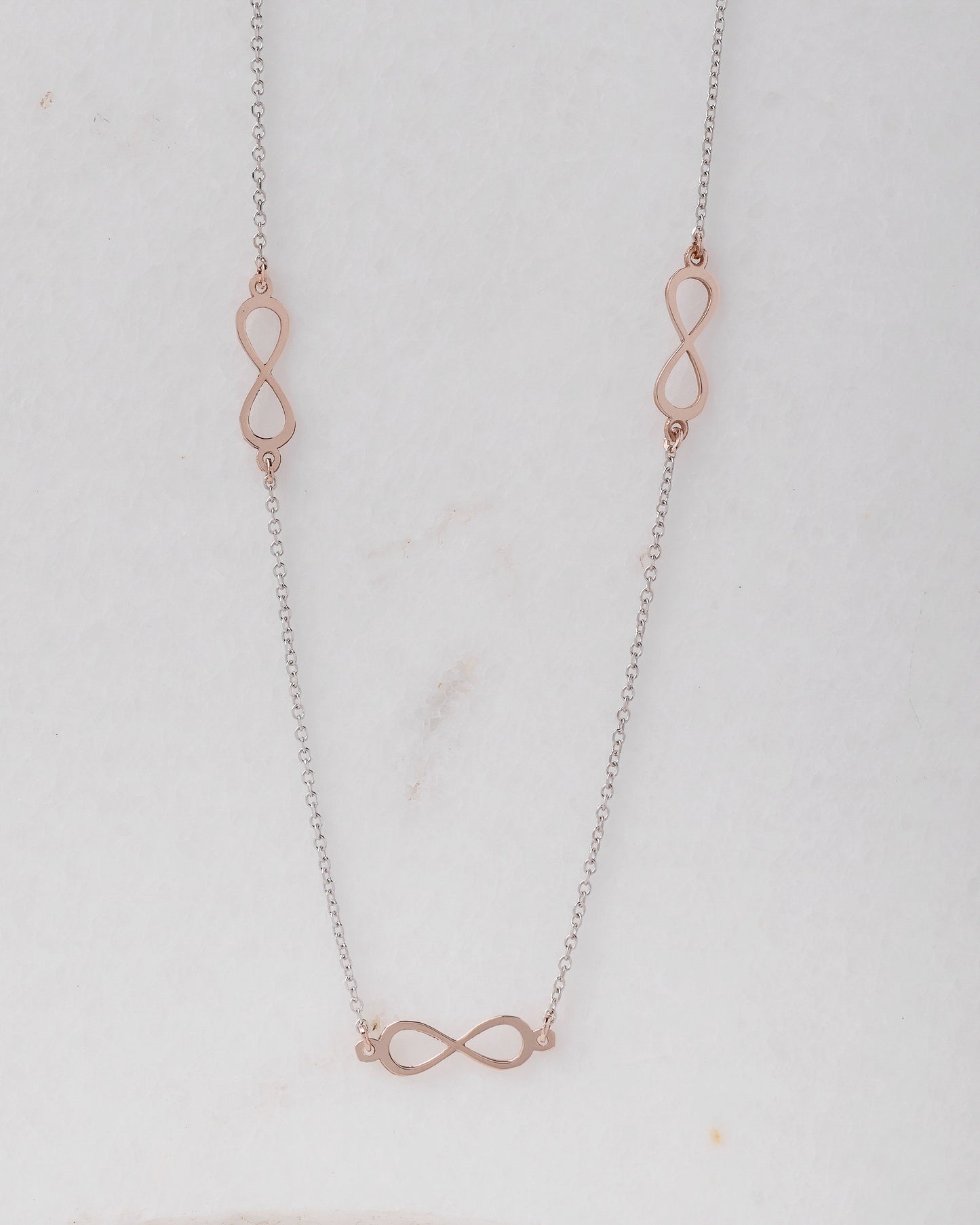 A station necklace featuring five infinity symbols in rose gold, complemented by a chain in white gold.