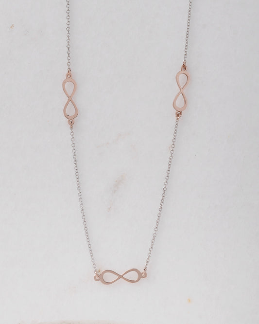 A station necklace featuring five infinity symbols in rose gold, complemented by a chain in white gold.