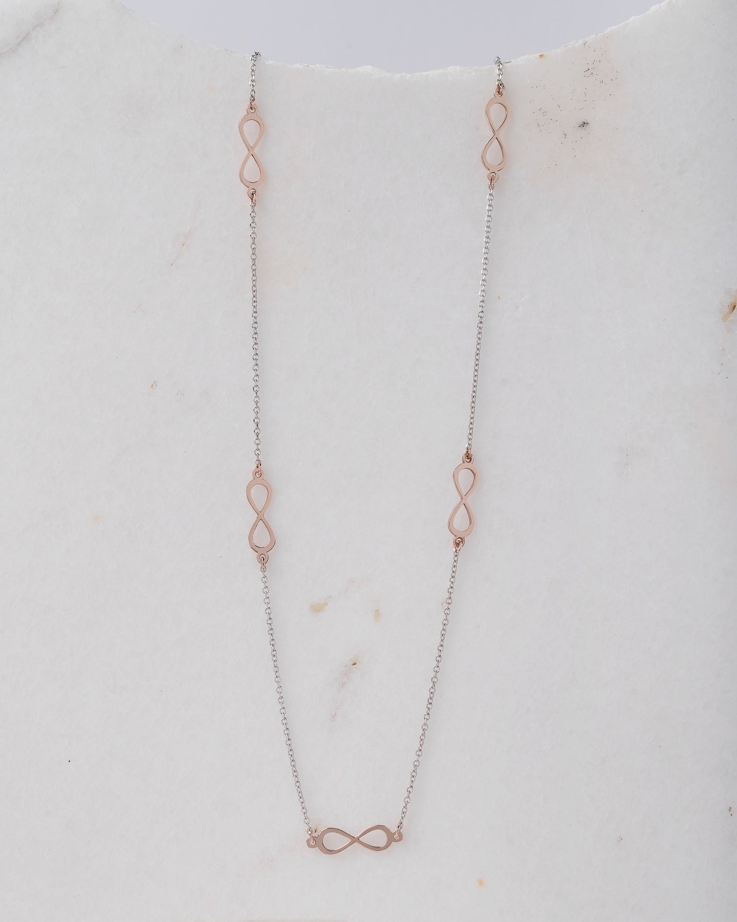 A station necklace featuring five infinity symbols in rose gold, complemented by a chain in white gold.