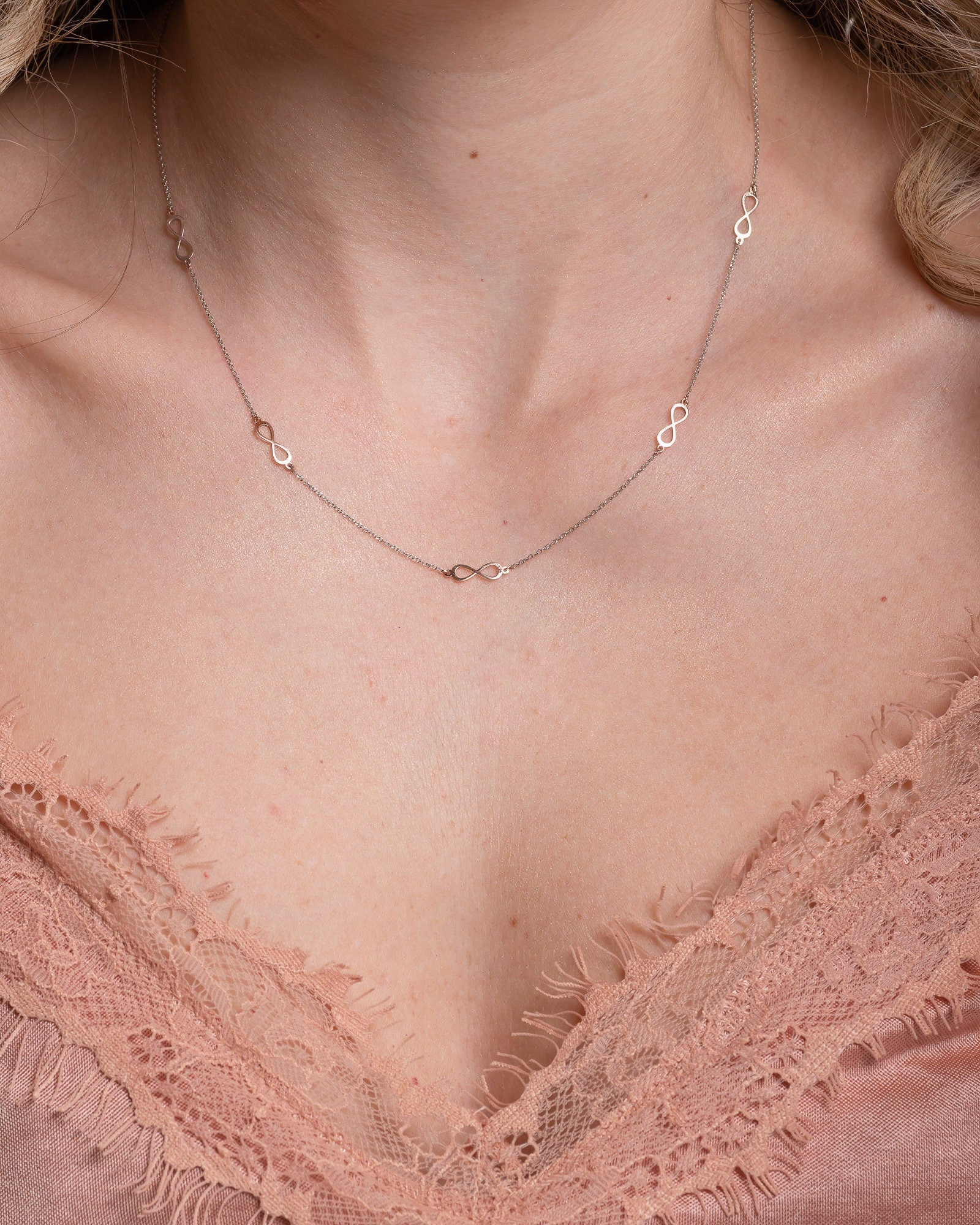 A station necklace featuring five infinity symbols in rose gold, complemented by a chain in white gold.