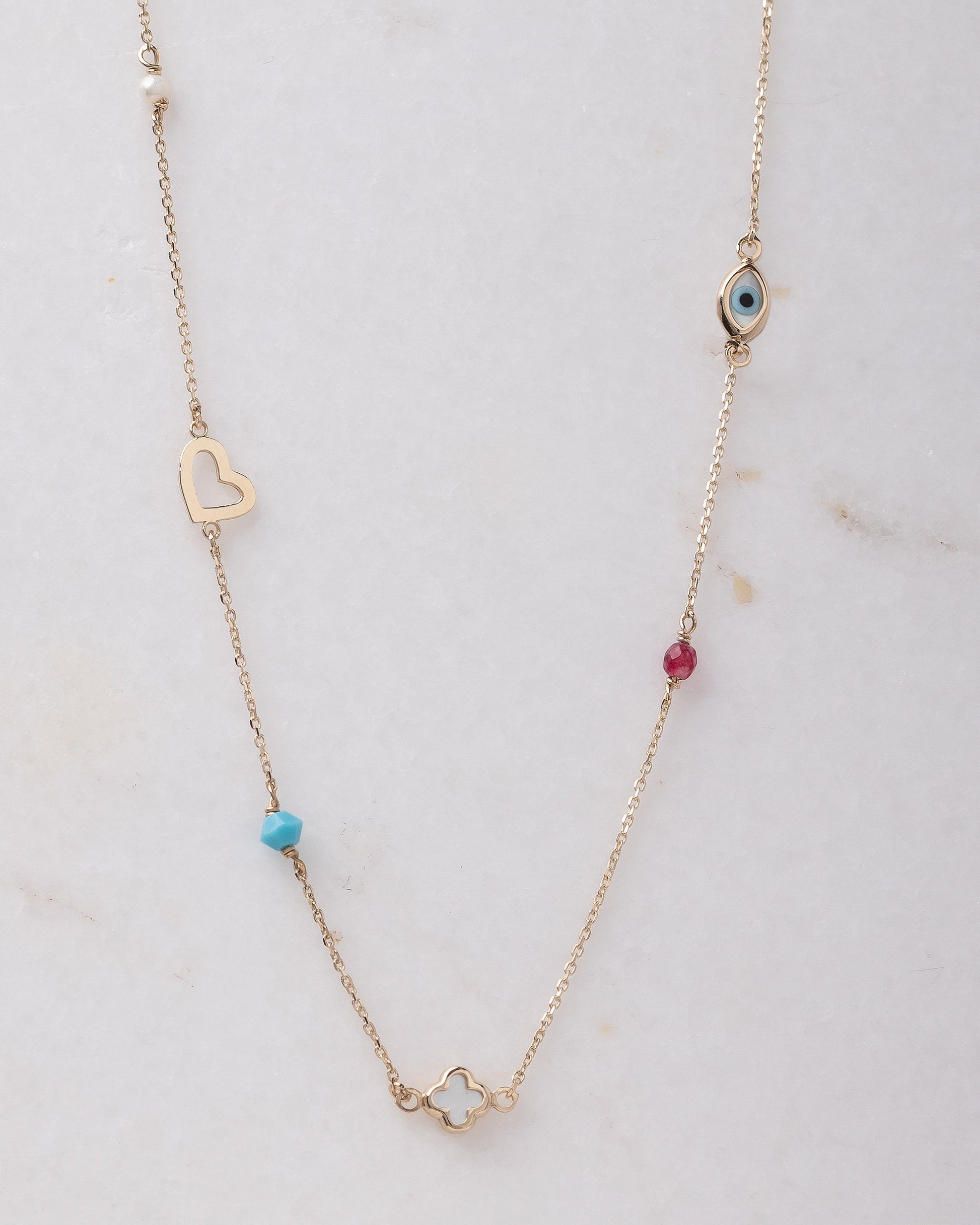 A station necklace featuring an evil eye, clover, heart, tourmaline, pearl, and turquoise stone set in 14k gold.