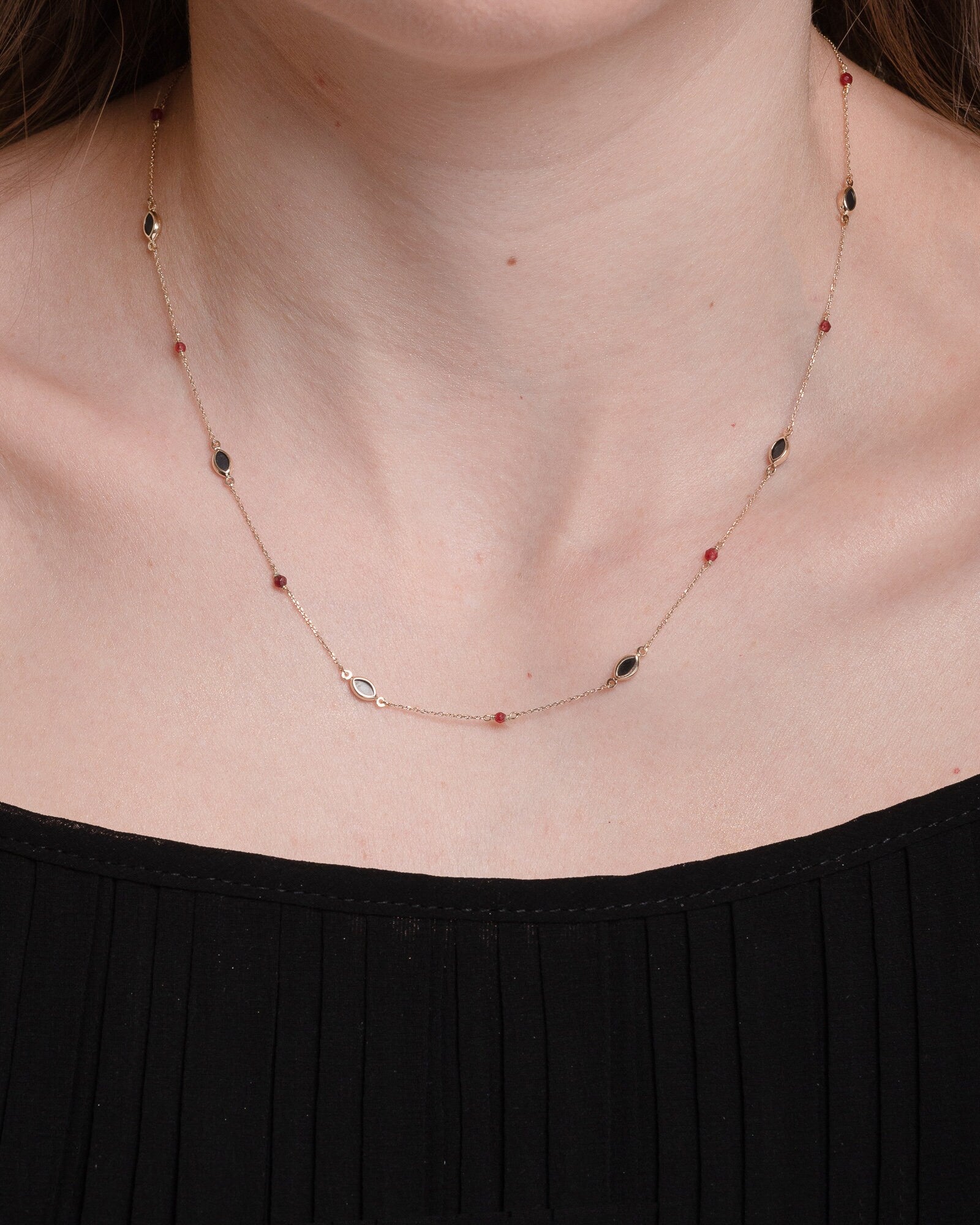 The photo shows a delicate gold necklace featuring small tourmaline gemstones and black marquise-shaped onyx accents, spaced along a fine chain. The contrasting colors create a striking and elegant design