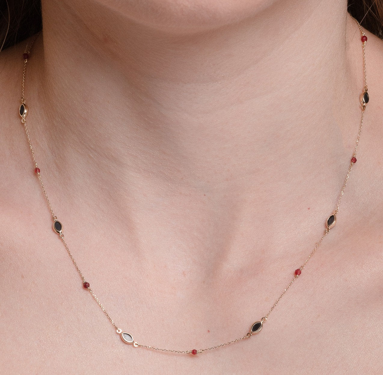 The photo shows a delicate gold necklace featuring small tourmaline gemstones and black marquise-shaped onyx accents, spaced along a fine chain. The contrasting colors create a striking and elegant design