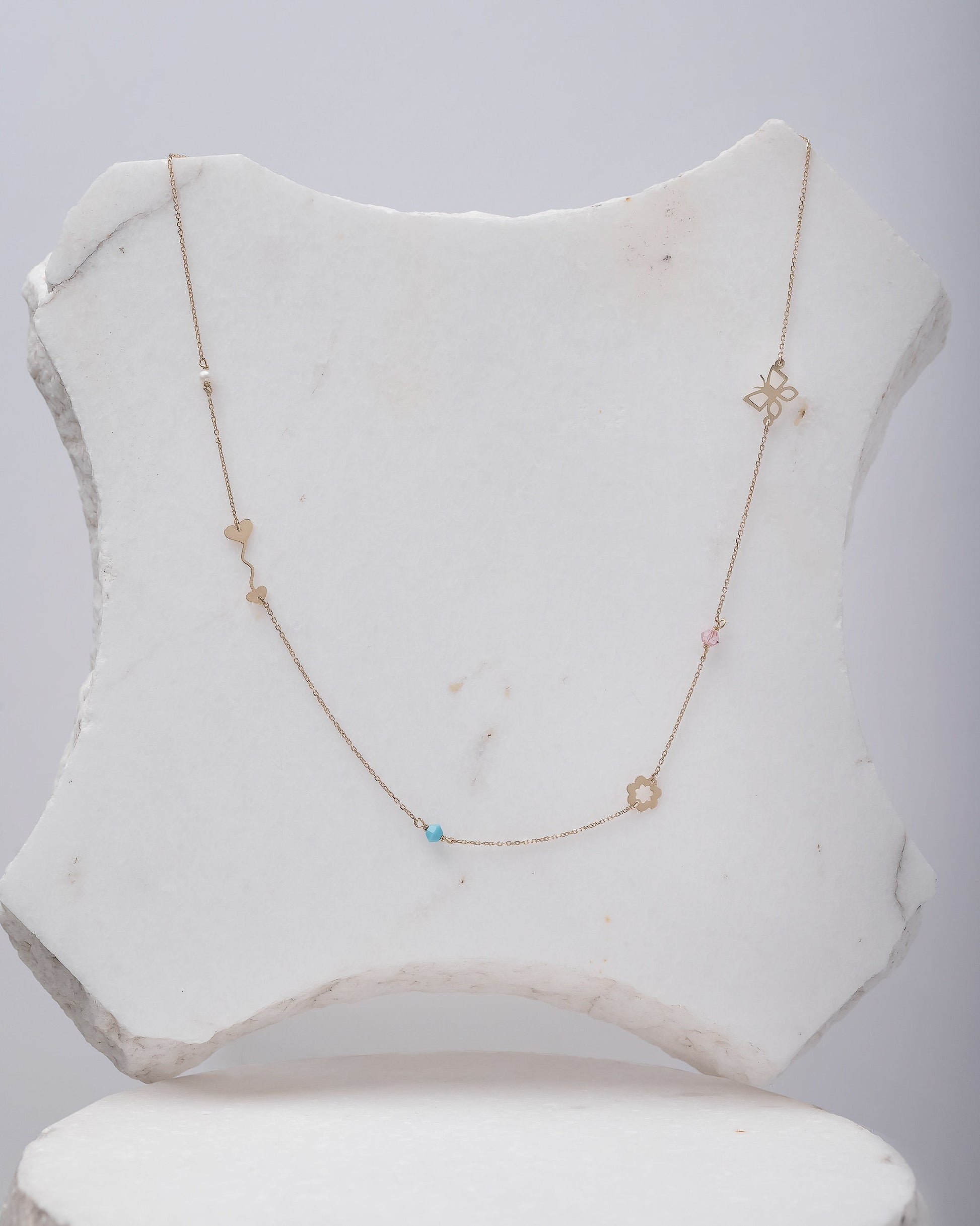 A station necklace featuring an arrow, flower, butterfly, pearl, turquoise, and a pink cubic zirconia stone.