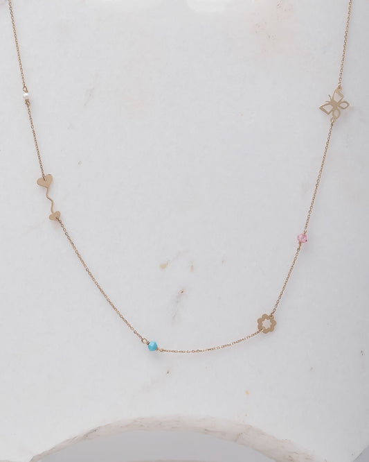 A station necklace featuring an arrow, flower, butterfly, pearl, turquoise, and a pink cubic zirconia stone.