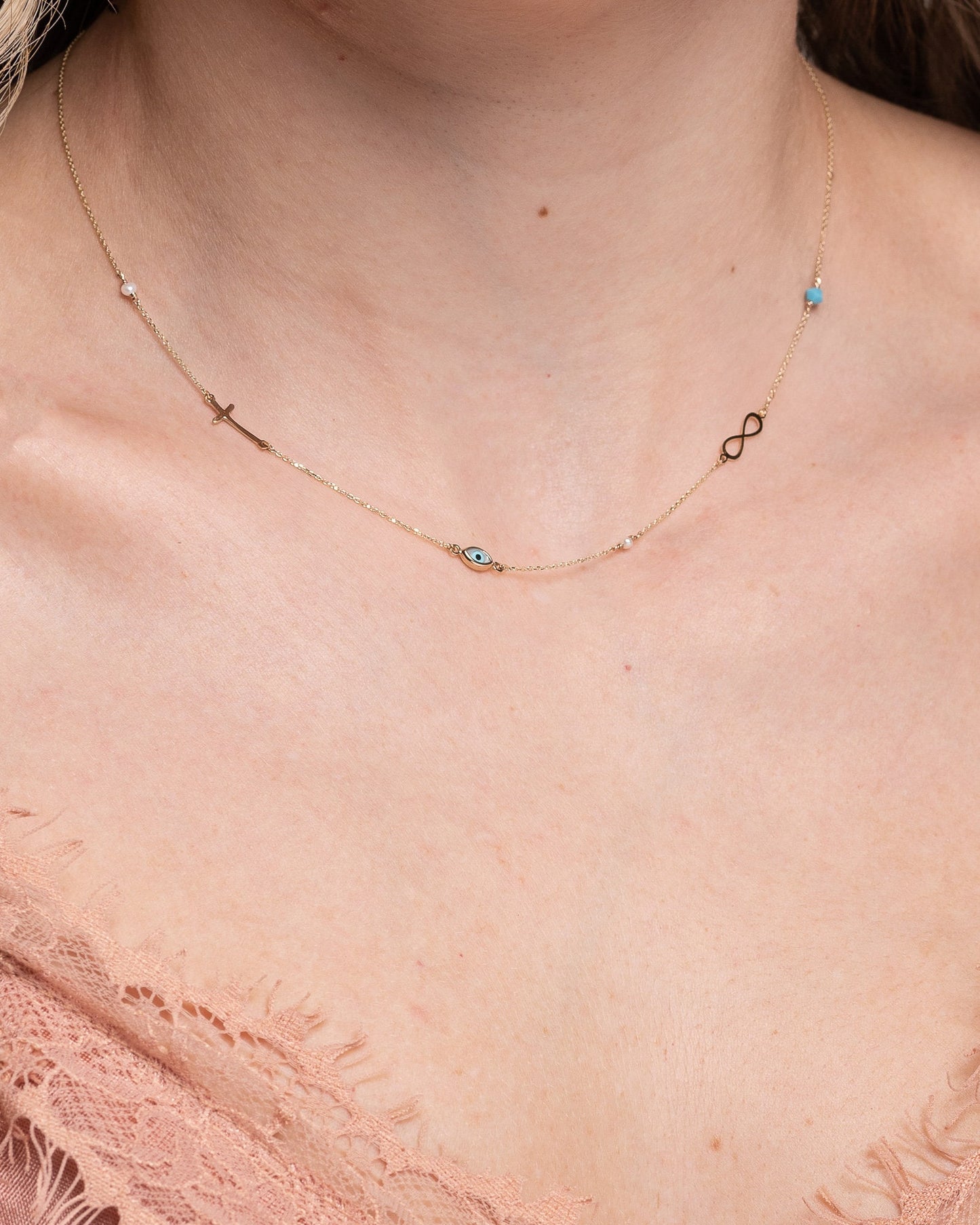 Station necklace featuring an evil eye, a cross, an infinity symbol, turquoise, and pearls in 14k gold.