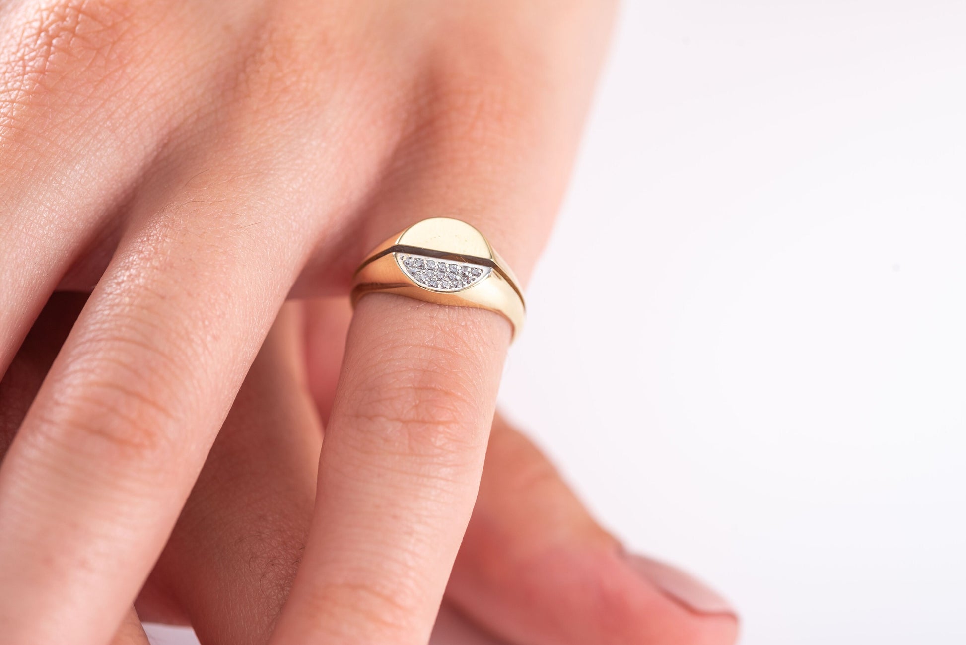 A round signet ring crafted in 14k gold, with half of the top part encrusted with white cubic zirconia stones.