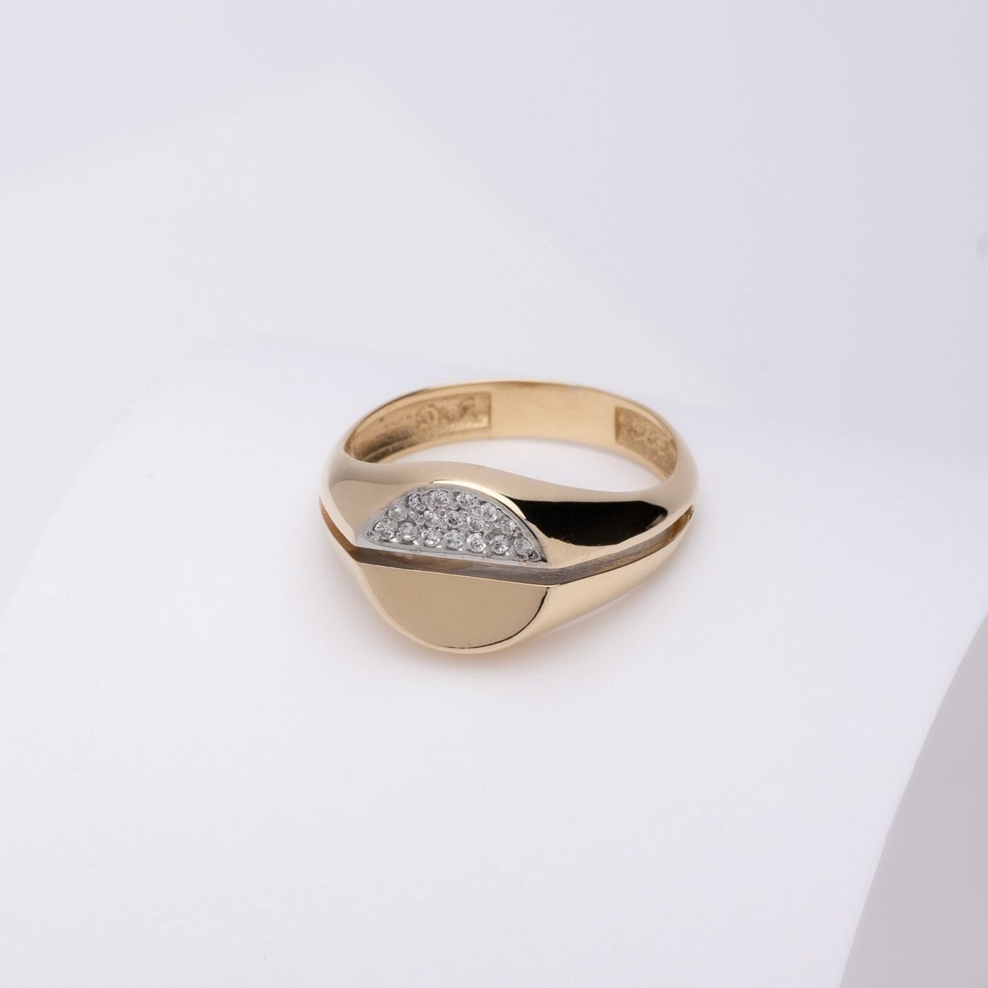 A round signet ring crafted in 14k gold, with half of the top part encrusted with white cubic zirconia stones.