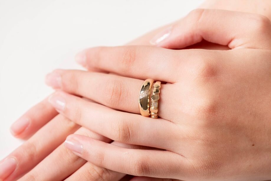 A hand adorned with two rings on the middle finger: one dome ring and one wrapped ring, both crafted in 14k gold.