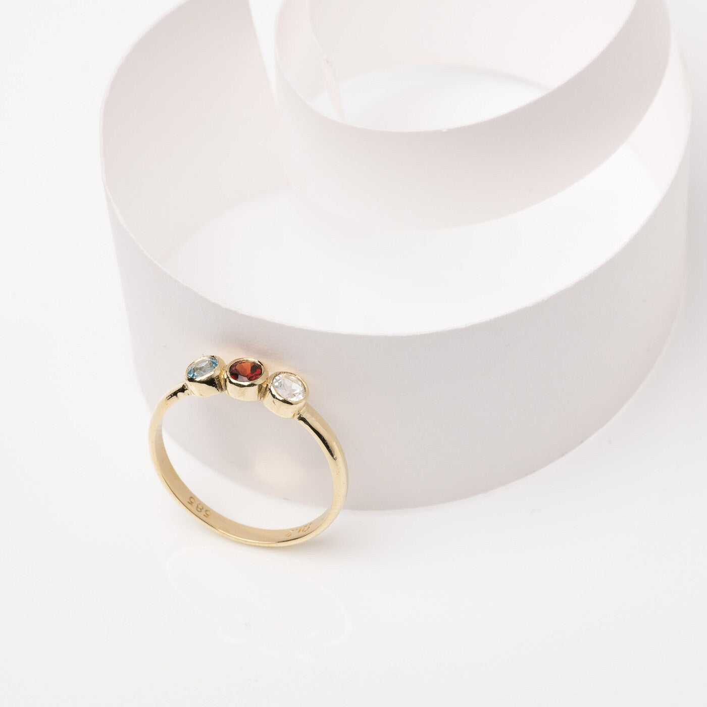 A handmade ring featuring three birthstones set in a bezel, crafted in 14k solid gold.