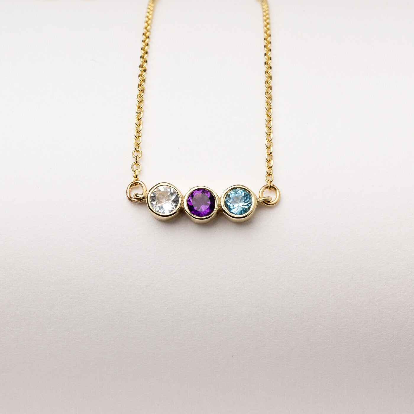 A 14k gold birthstone necklace for women, featuring three stones in a bezel setting.