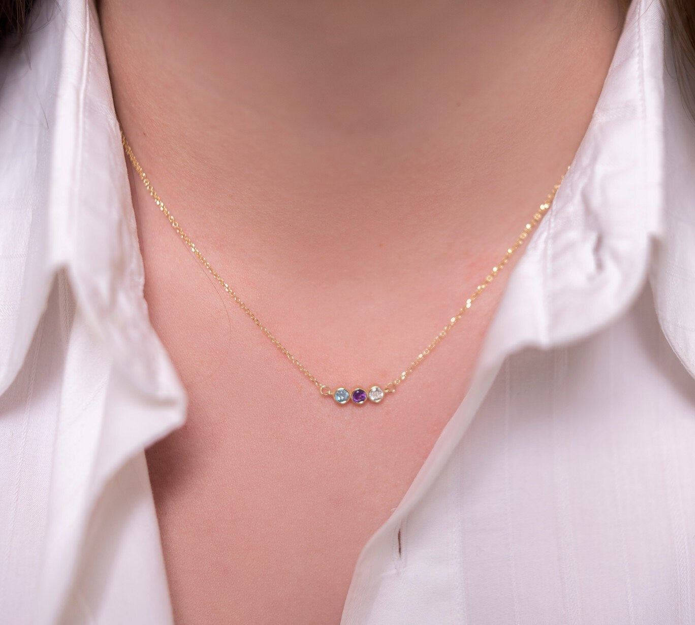 A 14k gold birthstone necklace for women, featuring three stones in a bezel setting.