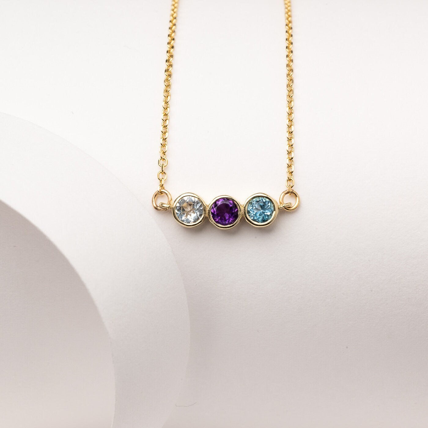 A 14k gold birthstone necklace for women, featuring three stones in a bezel setting.