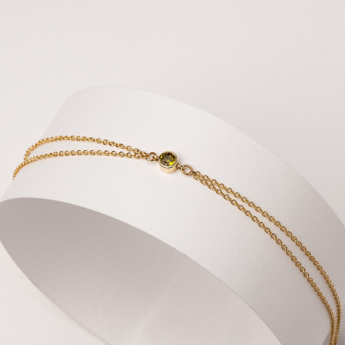 A handmade bracelet featuring a single birthstone in a bezel setting, crafted in 14k gold with a double chain design.