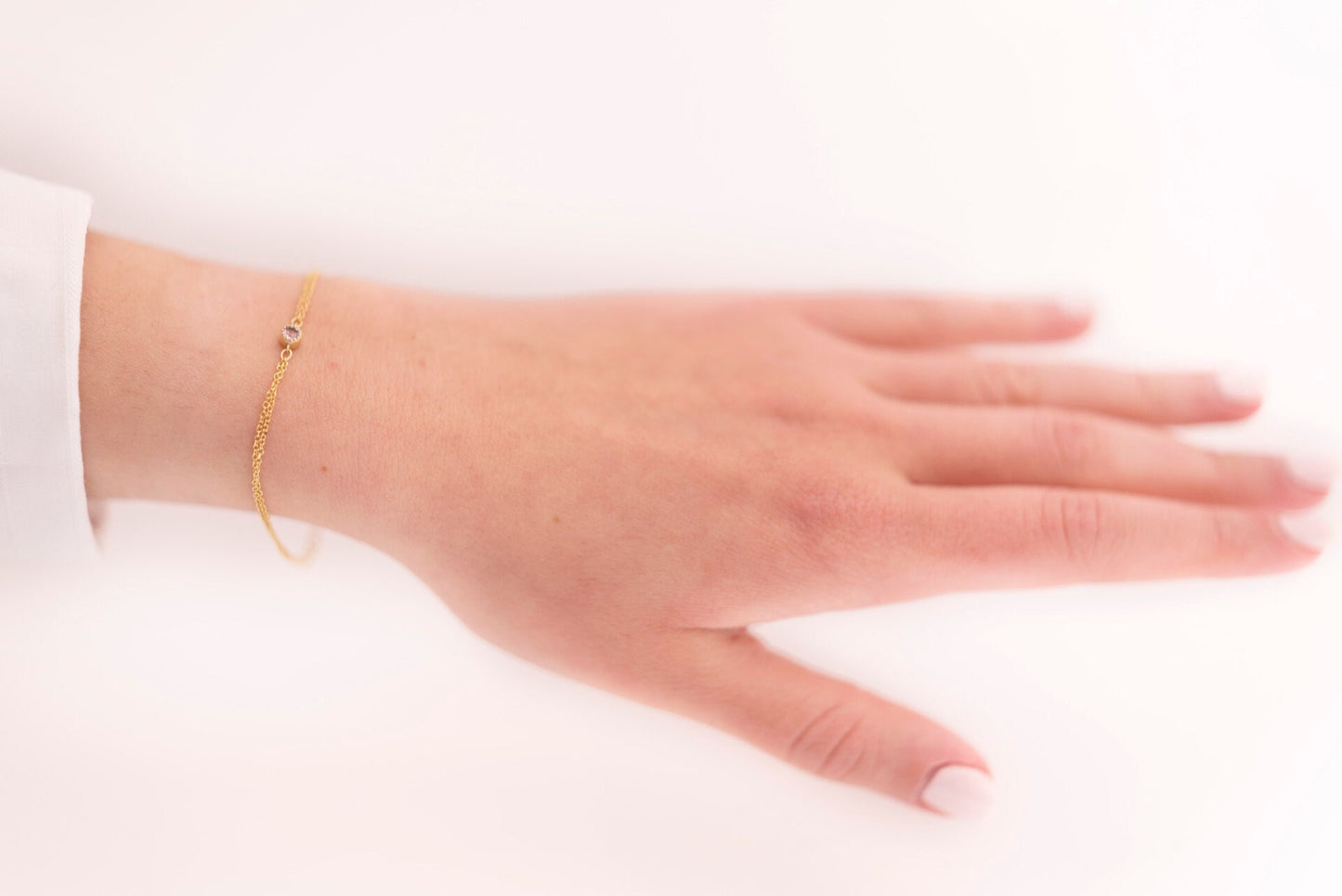 A handmade bracelet featuring a single birthstone set in 14k gold, complemented by a double chain design.