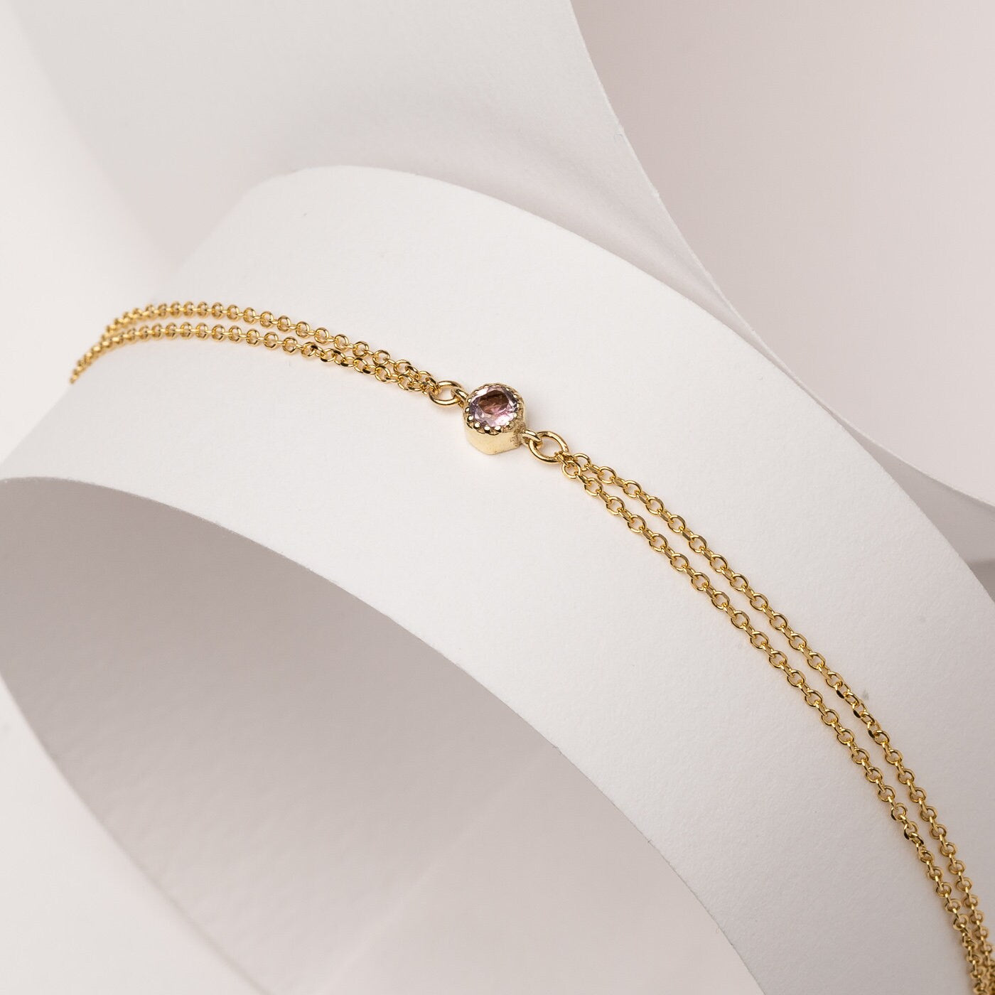 A handmade bracelet featuring a single birthstone set in 14k gold, complemented by a double chain design.