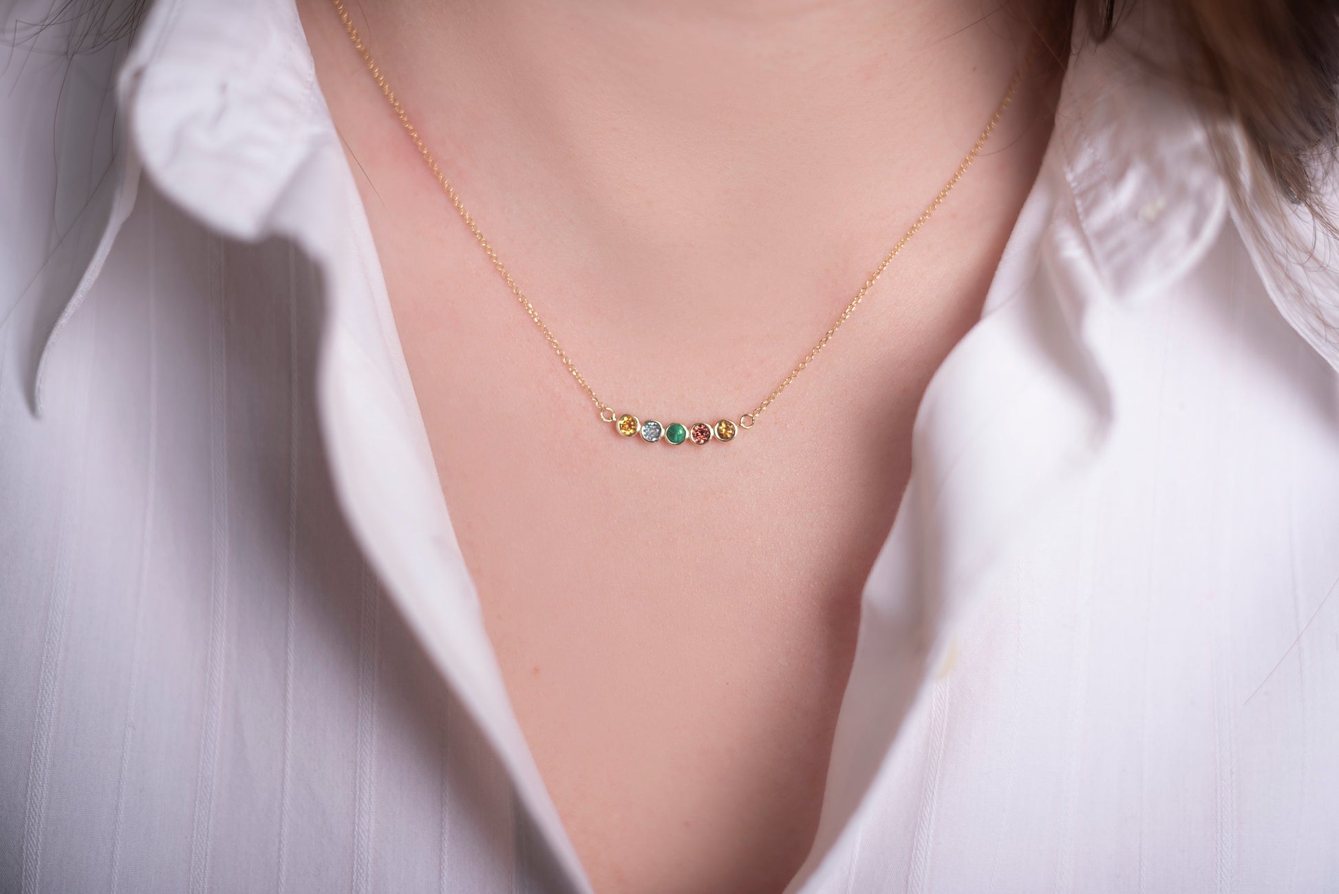 A 14k gold necklace for women, featuring five family birthstones.