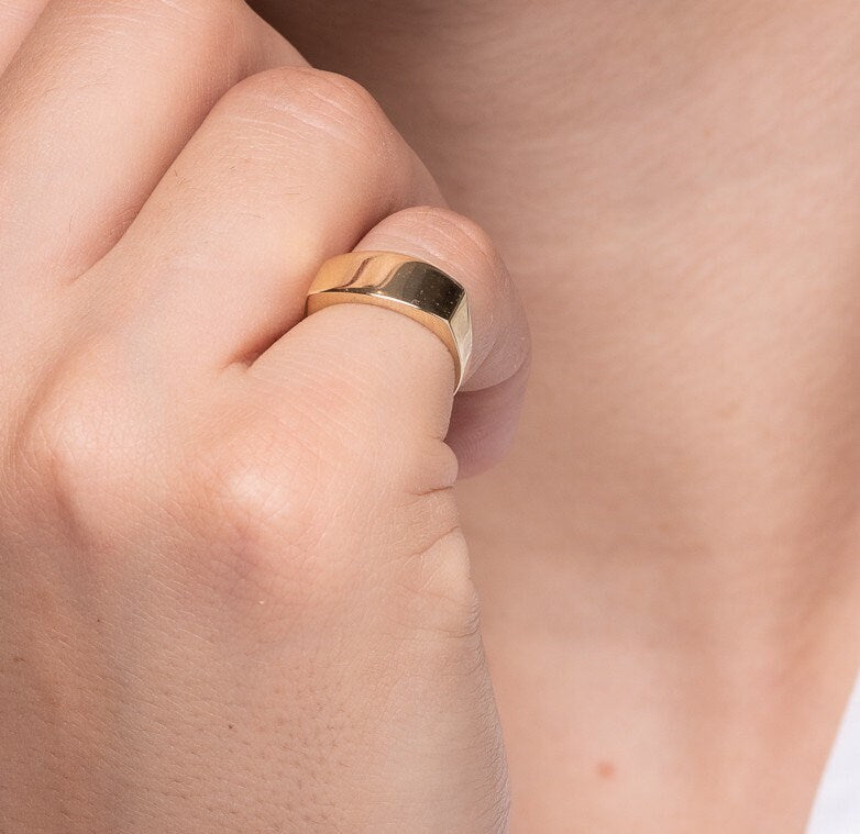 A personalized signet ring crafted in 14k gold, displayed on a model's pinky finger.