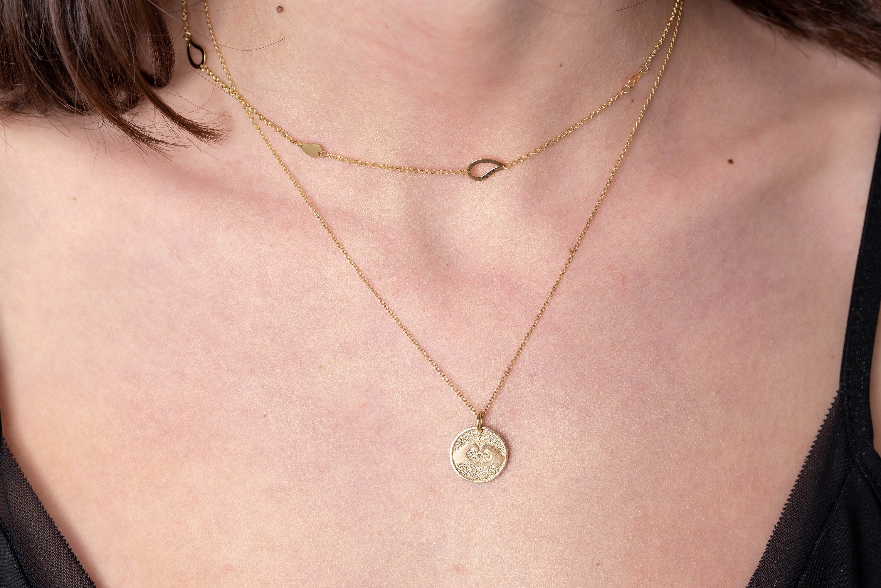 Hand Gesture Heart Necklace in 14k solid gold worn  by a model along with a station necklace with leaves